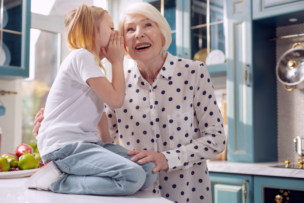 granddaughter whispering into ear of grandmother