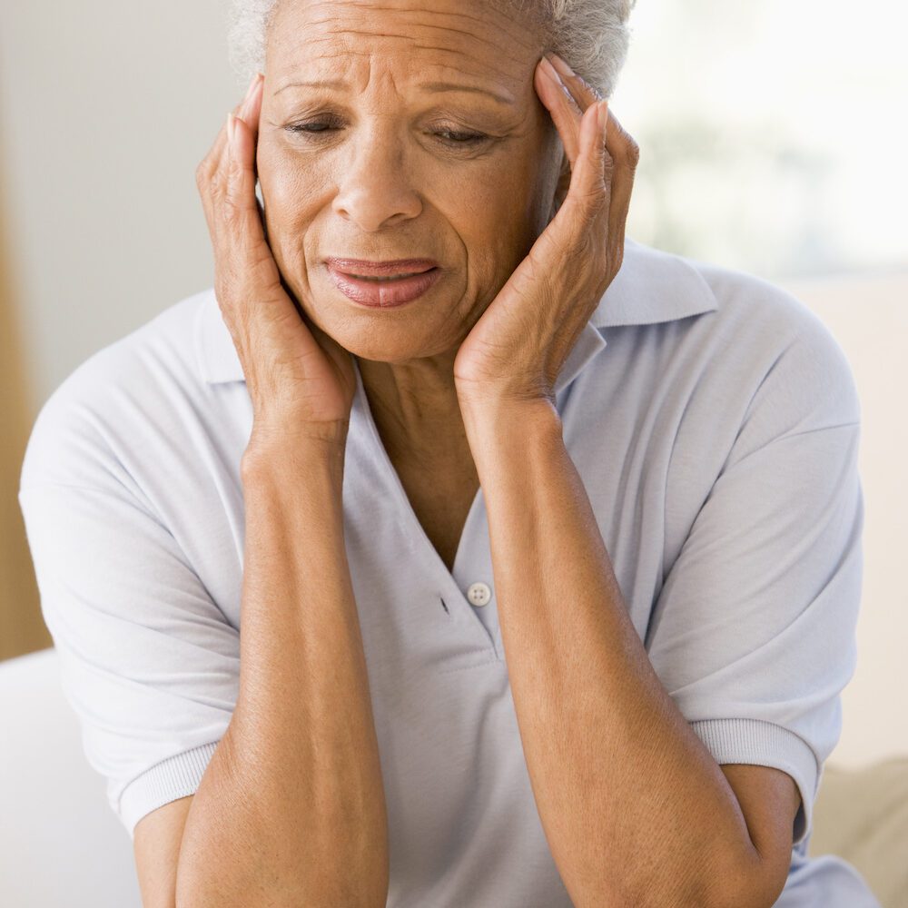 gray haired woman sitting down with head in hands due to pain