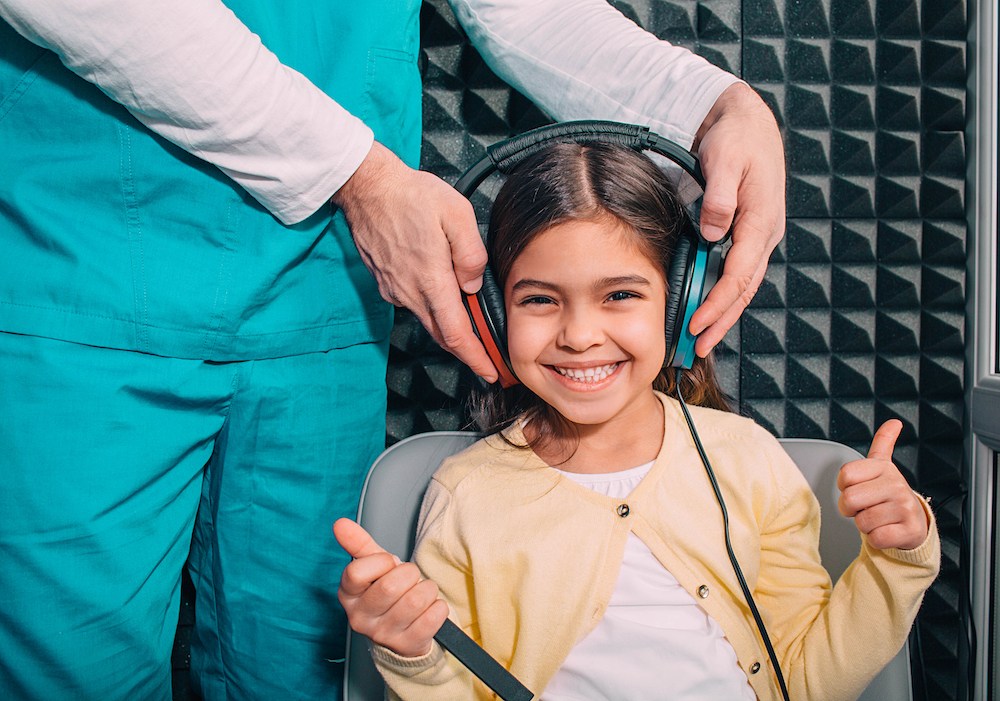 child smiling as her hearing specialist tests hearing in each ear