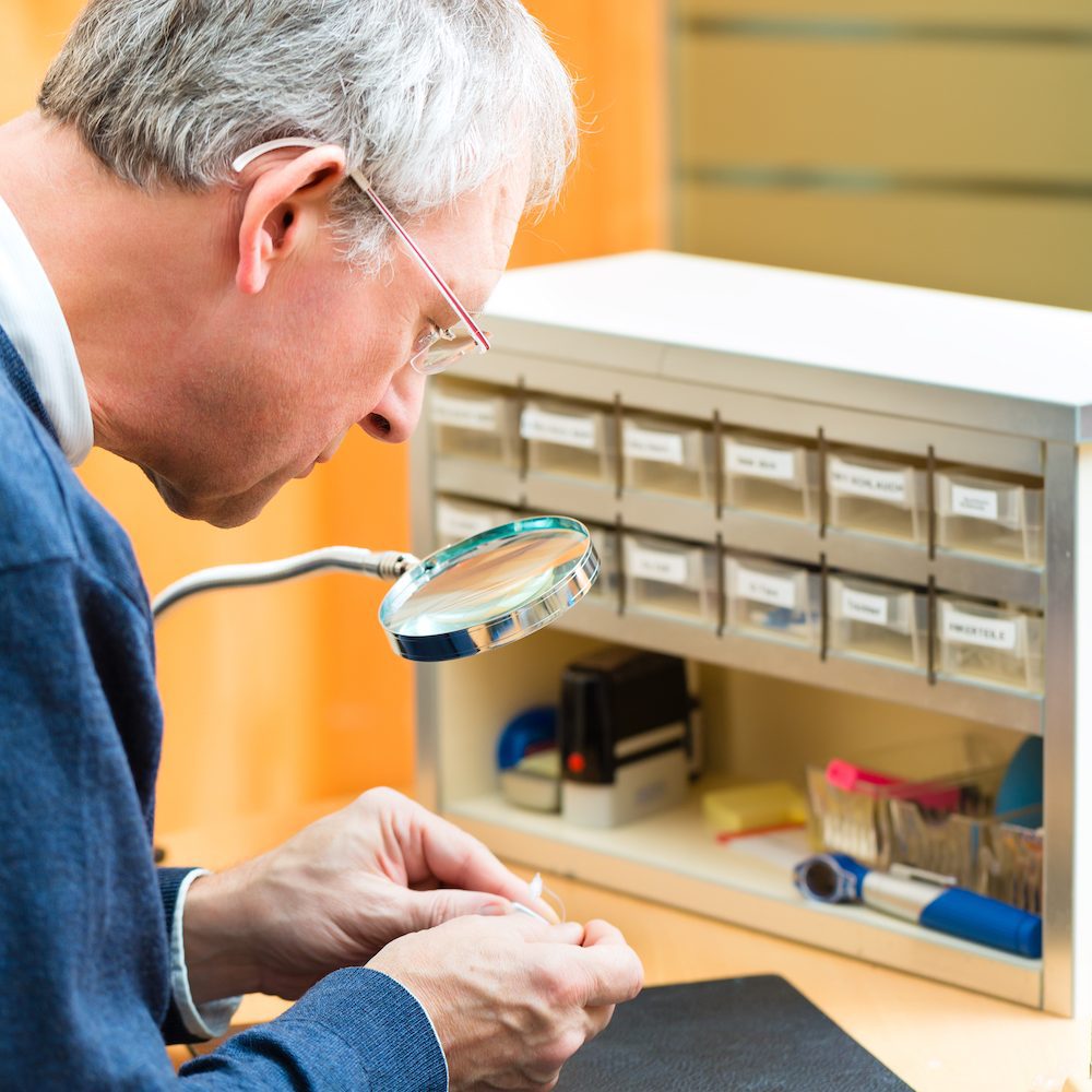 hearing specialist repairing a broken set of hearing aids