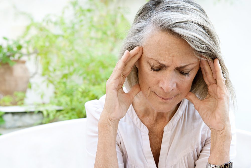gray haired woman with headache outside