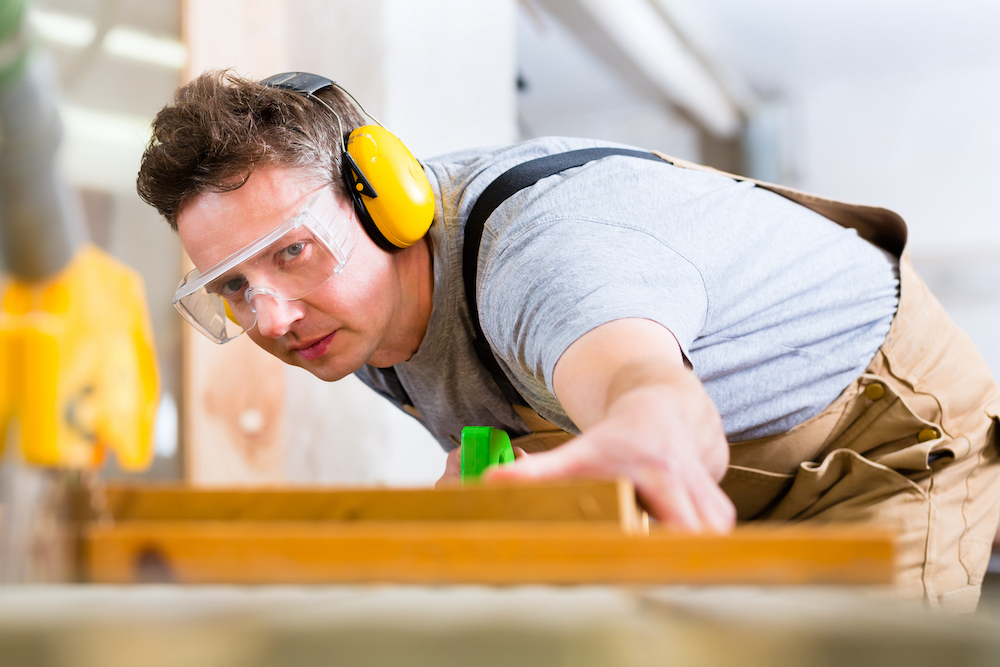 man cutting wood while wearing yellow over-the-head hearing protection