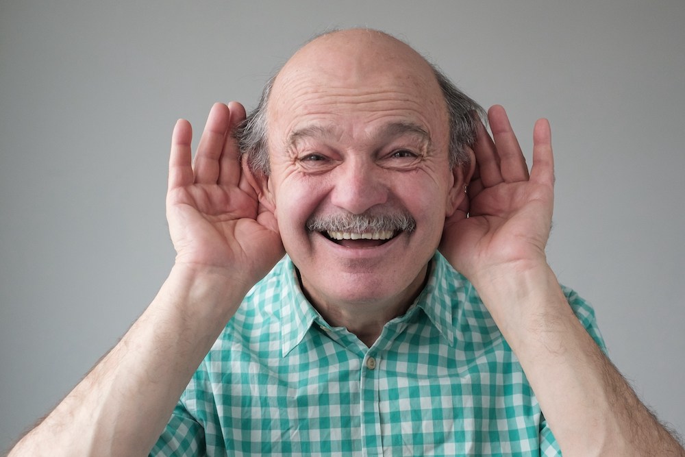 goofy looking man holding both hands to his ears optimized