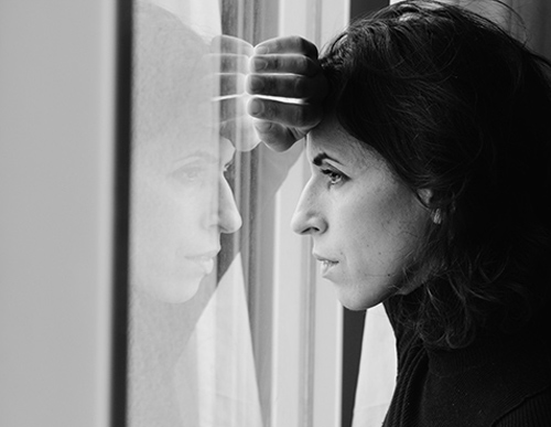 Black and white picture of sad woman looking out the window because of hearing loss.