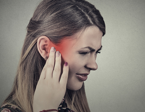 Woman holding her ear in pain from tinnitus