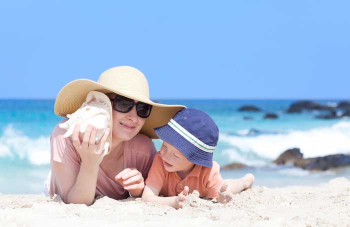 Older woman using shell as hearing aid to hear the surrounding ocean noise with her grandson.