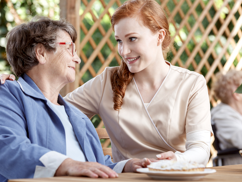 A young woman leans into an older woman to have a delicate conversation about hearing loss and hearing aids.