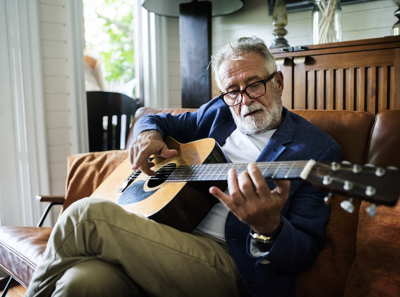 A man is playing guitar not realizing it may cause hearing loss as he is not wearing hearing protection.