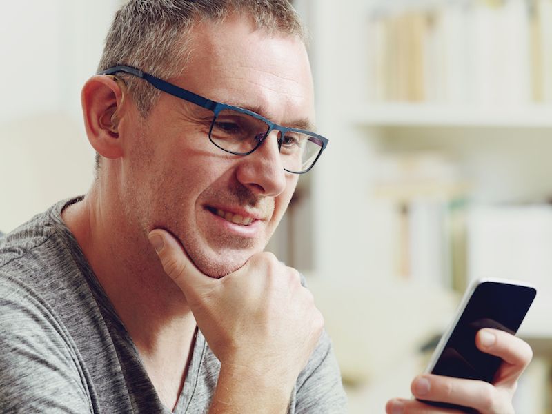 Man adjusting to new hearing aids by adjusting volume on his smartphone.