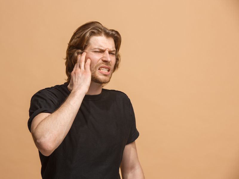 Man holding his ear because he has an ear infection that is causing hearing loss.