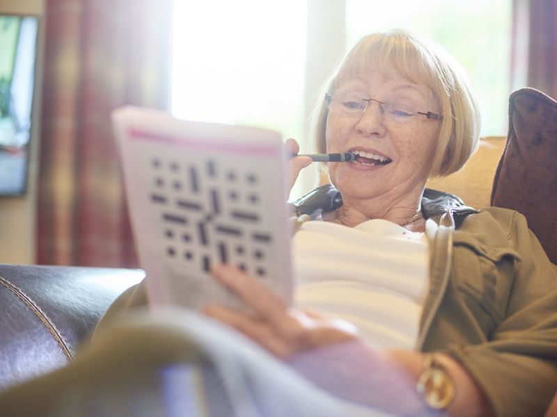 Woman doing crossword puzzle and wearing hearing aid to improve her brain.
