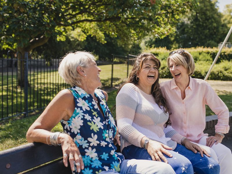Women with hearing loss laughing on park bench.