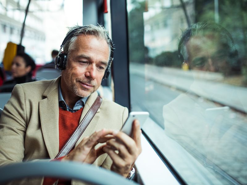 Man on bus wearing headphones unaware he is causing hearing loss with prolonged exposure.