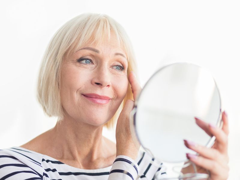 Woman puts her hearing aid in using a mirror to fight aging and age-related health issues like dementia.