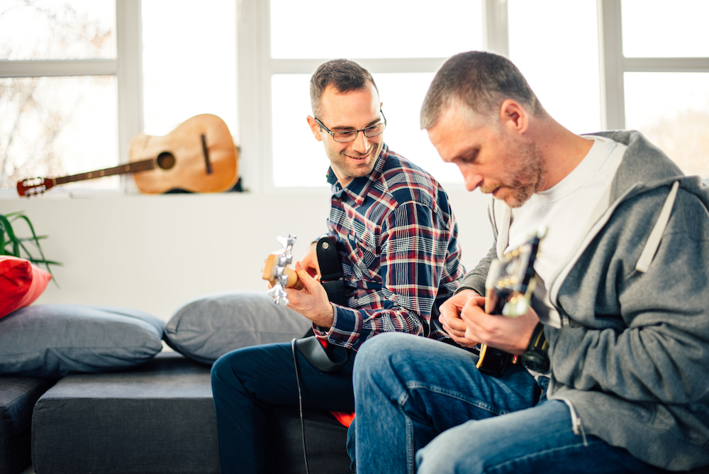 two musicians playing guitars on a couch