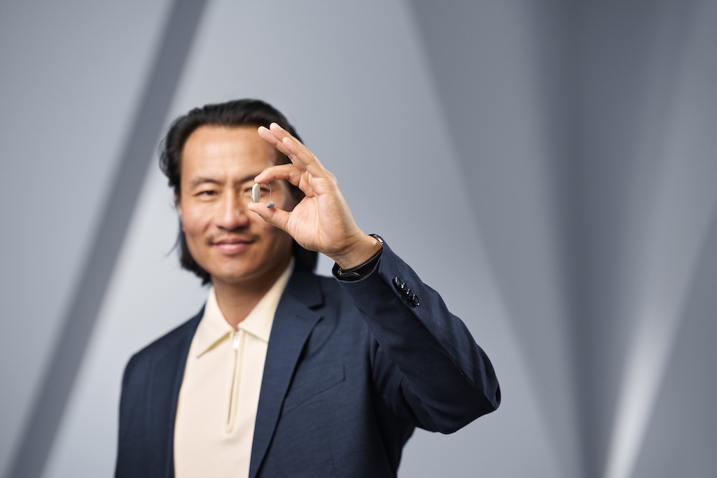 A person holding a silver ReSound Sensia receiver-in-ear hearing aid