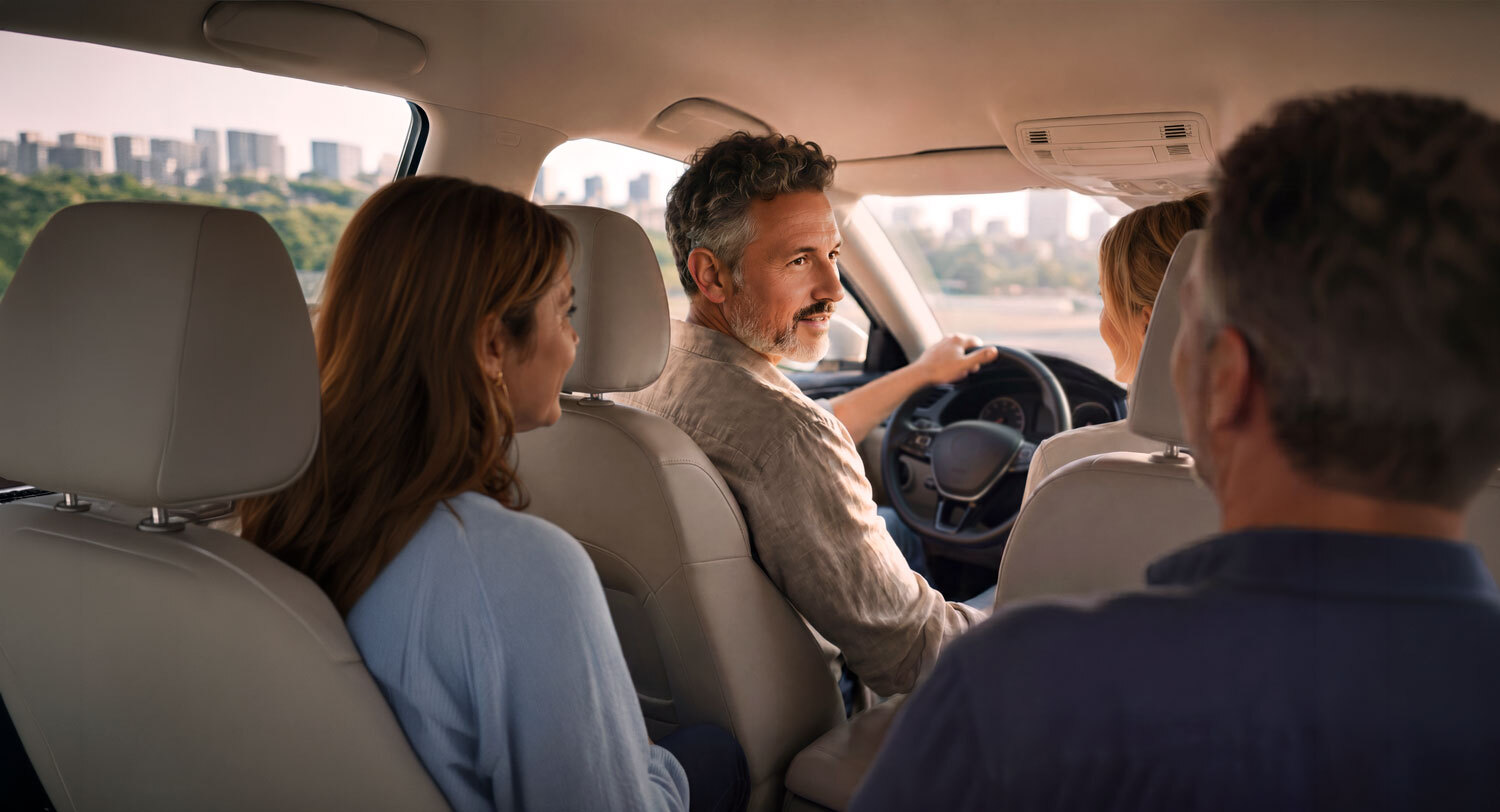 Four adults inside a car, one driving and three passengers engaged in conversation.