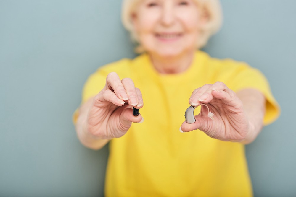 senior hearing loss patient in yellow shirt holding a hearing aid device in each hand