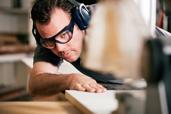 young man cutting wood in his garage while wearing hearing protection