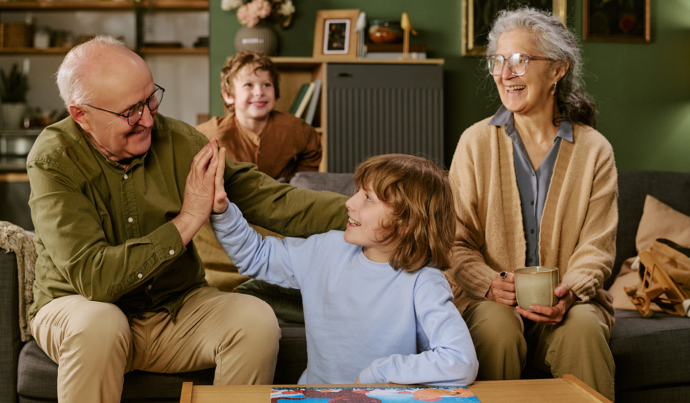 family grandson high fiving grandfather after completeing puzzle with grandmother and brother nearby