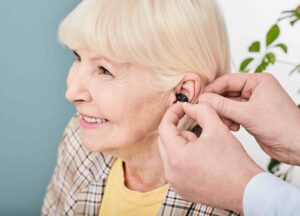 Audiologist inserting Intra-ear hearing aid to senior woman patient, close-up. Hearing solution for elderly people