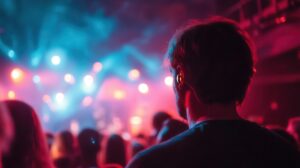 A man wearing earplugs watches a vibrant concert, surrounded by colorful stage lights and a lively crowd