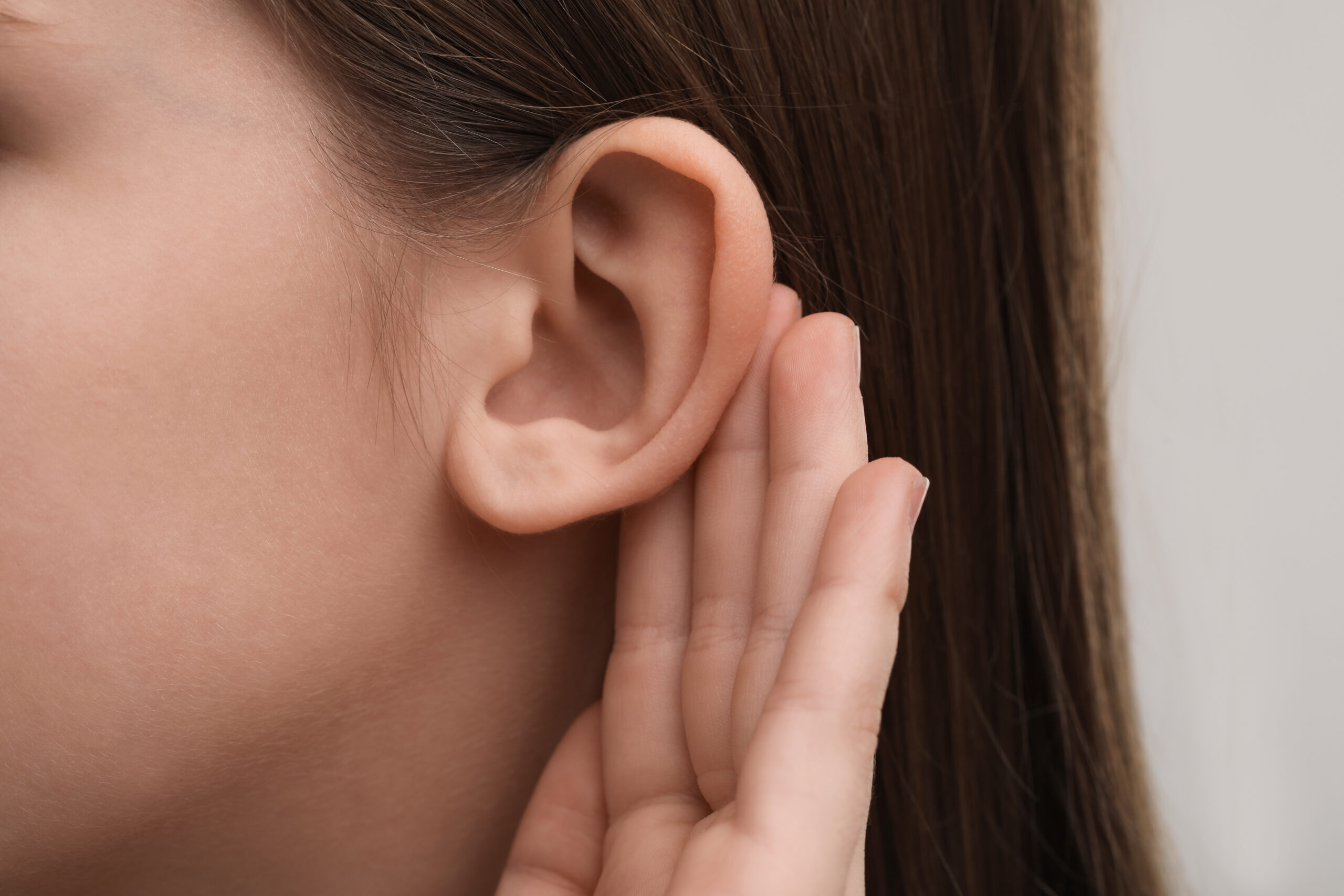 Little girl with hearing problem on grey background, closeup