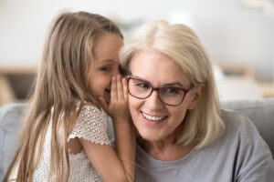 Cute little granddaughter whispering in ear telling secret to gr
