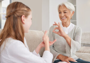 Senior woman, sign language and deaf girl communication, talking or conversation in home Support, care and retired old female speaking to child with hearing disability in asl language hand gestures