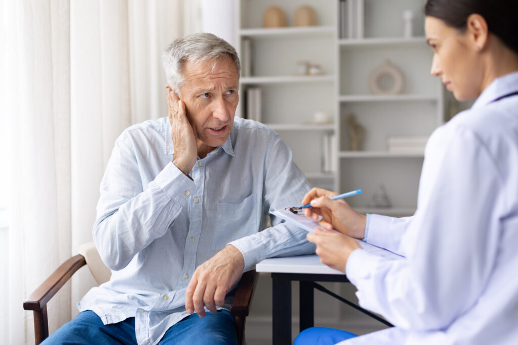 Senior male patient reporting ear pain to female doctor during medical visit