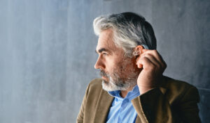 Grey haired mature man with hearing impairment using hearing aid Hearing solutions for deafness people