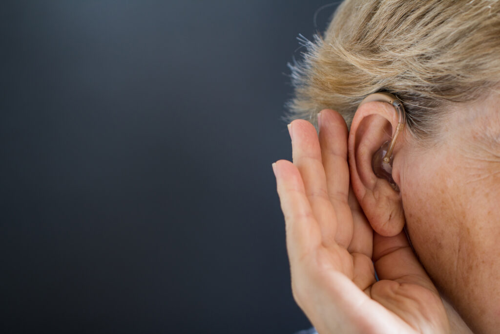 Elderly woman with hearing aid on grey background Deafness concept