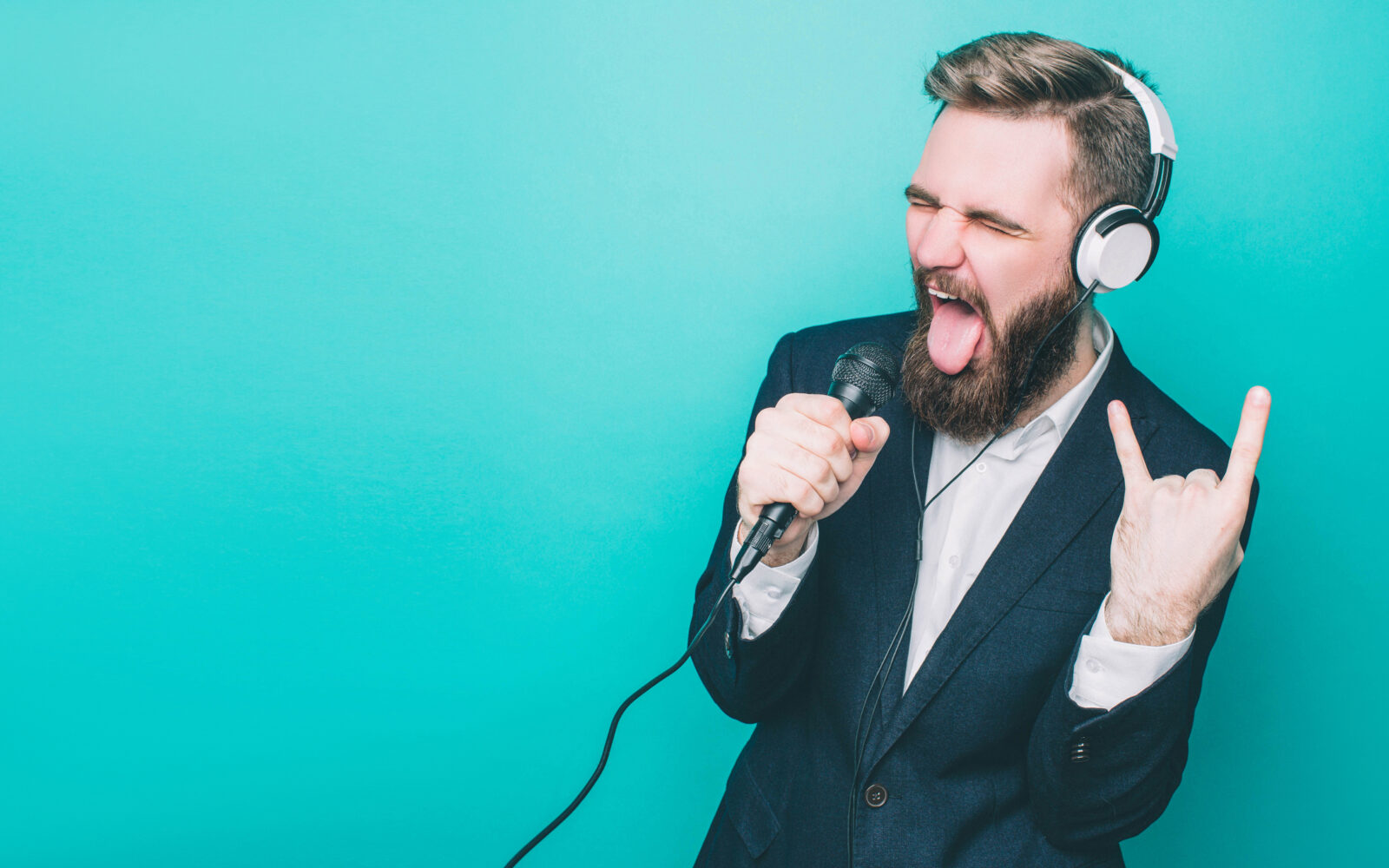 Guy is rocking out He has the headphones and singing in microphone Also he is showing the rock symbol with his hand Isolated on blue background