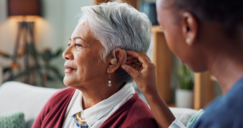 Nurse, woman and hearing aid on ear for medical support, wellness and innovation of disability People, healthcare worker and deaf patient with audiology implant, service or help for sound waves