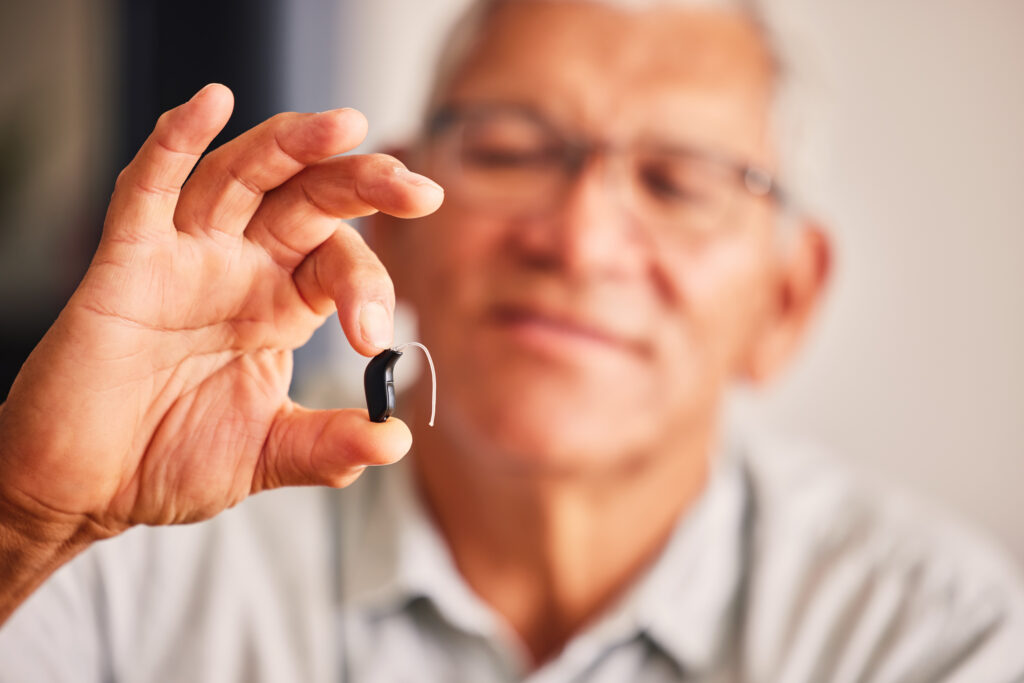 Hand holding hearing aid, senior man and tech for ears, health and wellness for retirement in nursing home Elderly person with disability, audio or sound technology to listen in closeup at house