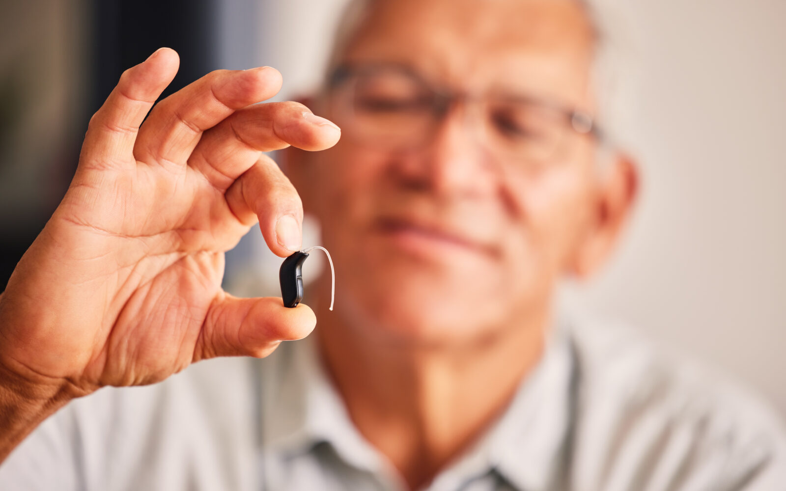 Hand holding hearing aid, senior man and tech for ears, health and wellness for retirement in nursing home Elderly person with disability, audio or sound technology to listen in closeup at house