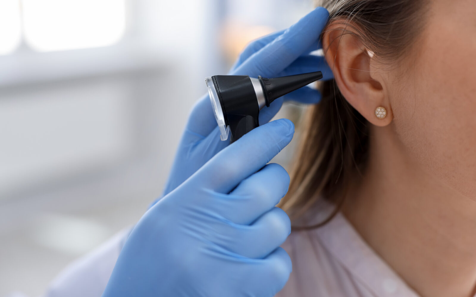 Hearing test Doctor examining woman's ear with otoscope in clinic, closeup Space for text