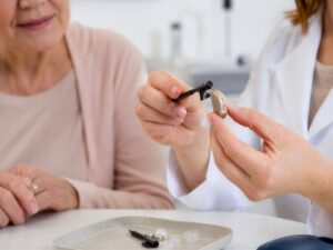 Audiologist cleaning hearing aid for senior woman Medical specialist demonstrating maintenance of assistive device in clinic Healthcare professional helping patient with hearing loss