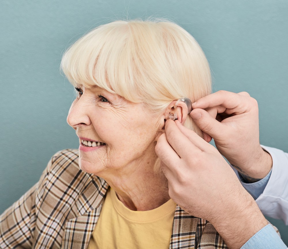 senior hearing loss patient smiling as she is fitted with a brand new hearing aid