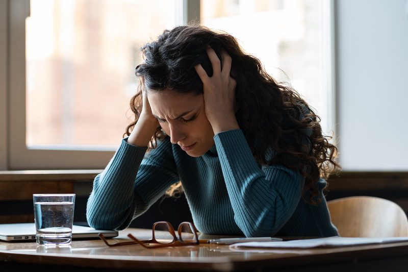 Unhappy female overworked and stressed sit at desk with closed laptop suffer from headache, depression feeling exhausted frustrated with bad news, failure at work. Tired sick woman worker in office