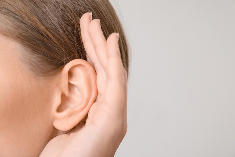 Young woman with hearing problem on light background, closeup