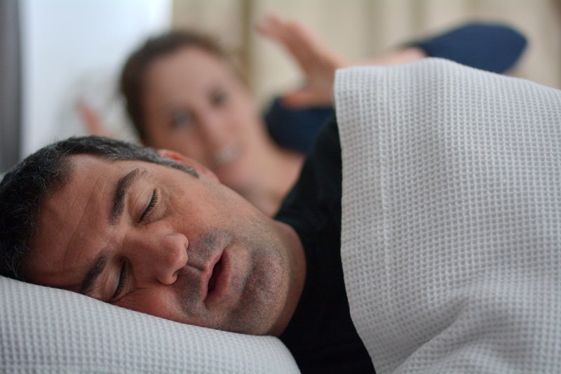 Woman (age 30) suffers from her male partner (age 40) snoring in bed. Noise concept. Real people. Copy space