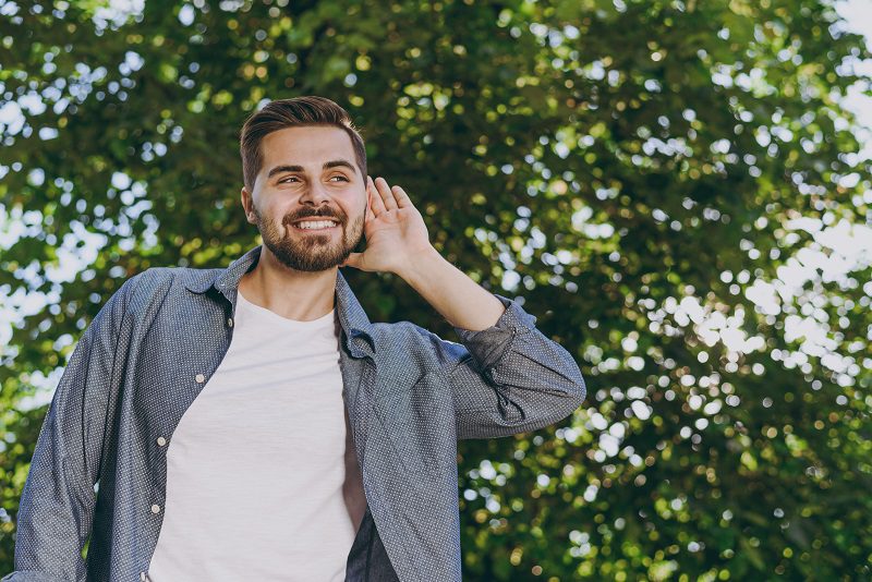 Young smiling satisfied man in blue casual shirt walk listening chirping birds rest relax in spring sunshine forest green city park go down alley outdoors on nature Urban lifestyle leisure concept.