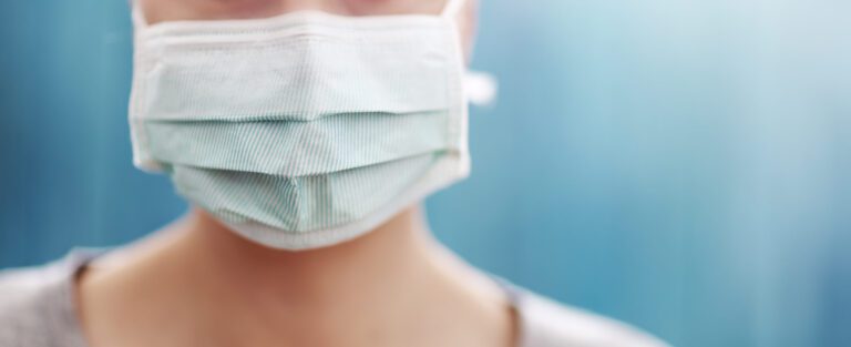 young woman in medical face protection mask indoors on blue background. Sick person