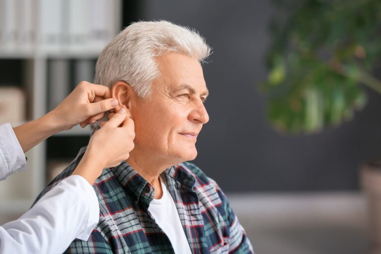 Doctor putting hearing aid in mature man's ear in clinic
