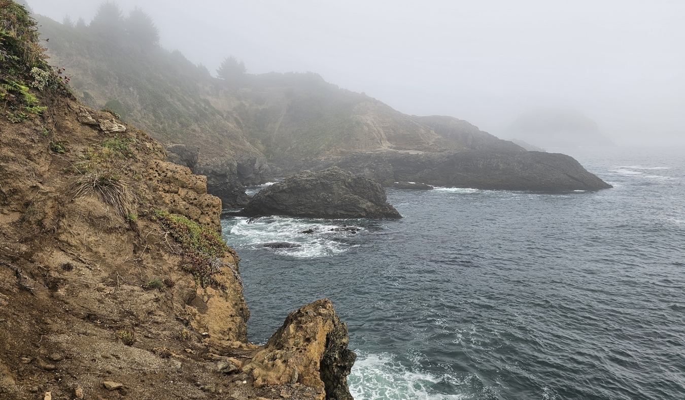 california rugged coastline juts out into the misty Pacific with waves crashing against the cliffs