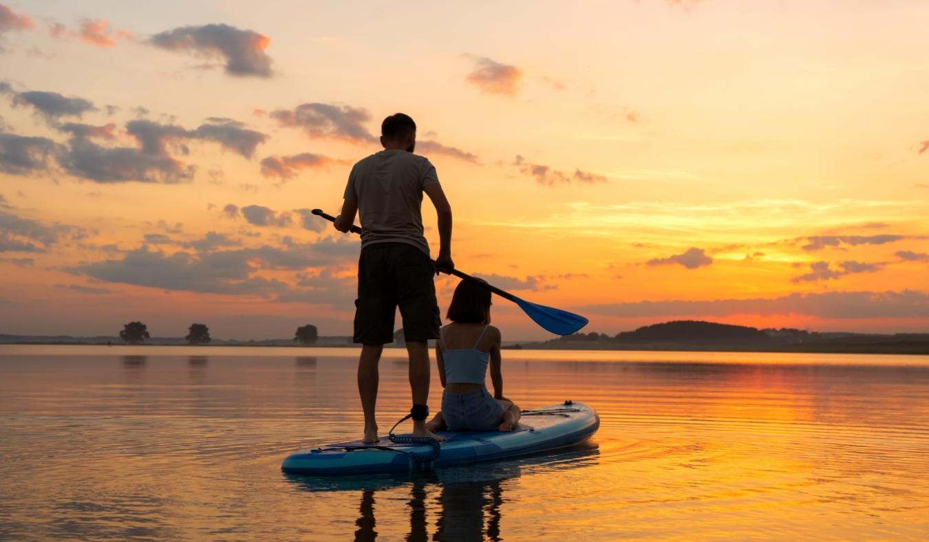 couple paddleboarding at lake during sunset together