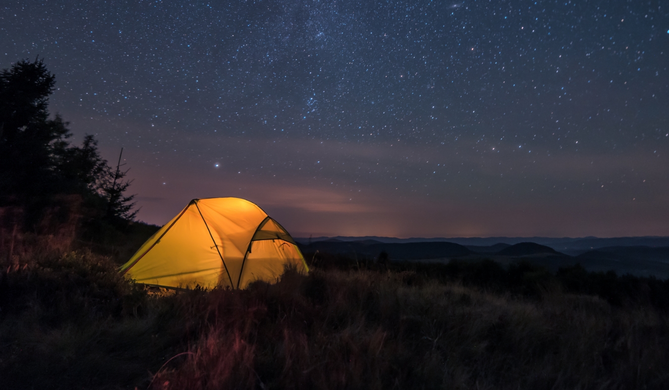 iluminated tent under stars in the mountains