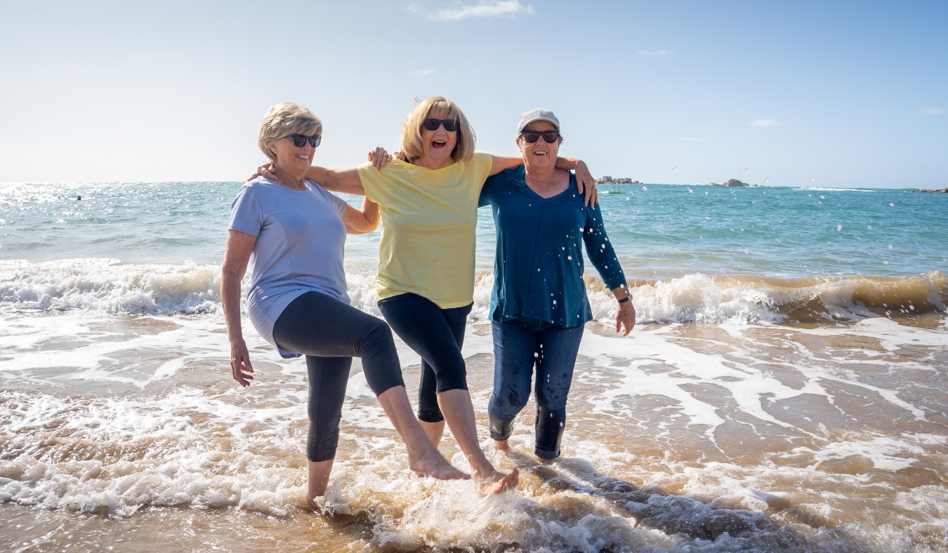 Lovely group of senior girl friends walking and having fun splashing water on sea