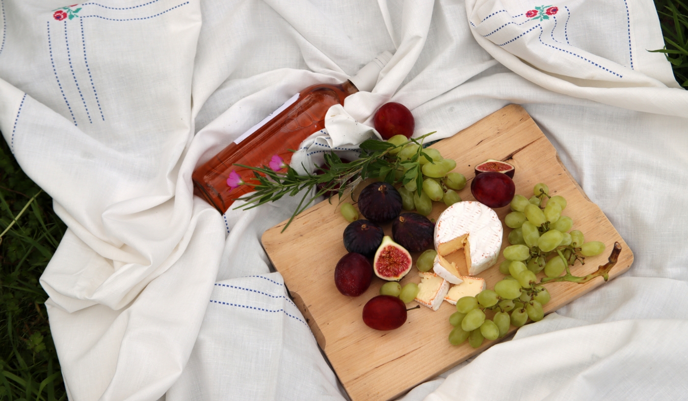 picnic with wooden board with figs grapes cheese and plums bottle of rose wine
